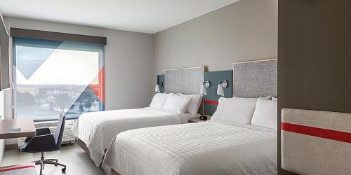 费耶特维尔avid hotel Fayetteville West的酒店客房设有两张床、一张书桌和一个窗户。