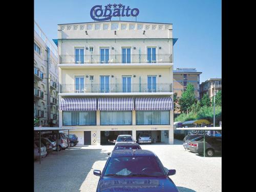 里米尼克巴尔托酒店的一座大型建筑,前面有汽车停放