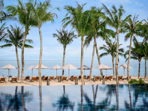 富国New World Phu Quoc Resort的海滩上的游泳池,种植了棕榈树和遮阳伞
