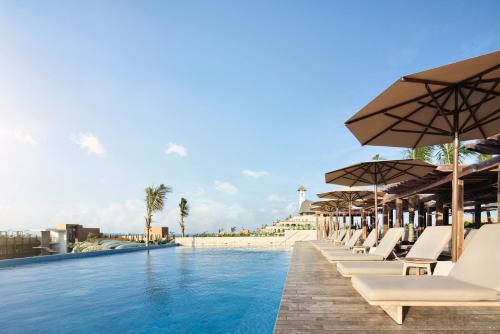 普拉亚卡门Hotel Xcaret Arte - All Parks All Fun Inclusive - Adults Only的一个带椅子和遮阳伞的游泳池以及一个海滩