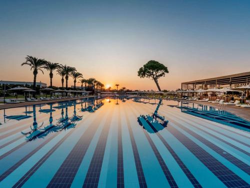 贝莱克Rixos Premium Belek - The Land of Legends Access的棕榈树和日落的游泳池