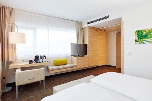 萨尔茨堡H+萨尔茨堡酒店 的酒店客房设有一张床、一张书桌和一台电视机。