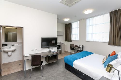 新普利茅斯奎斯特新普利茅斯服务式公寓的酒店客房配有床、书桌和水槽