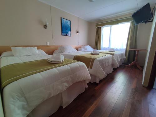 纳塔列斯港HOTEL GLACIARES的酒店客房设有三张床和窗户。