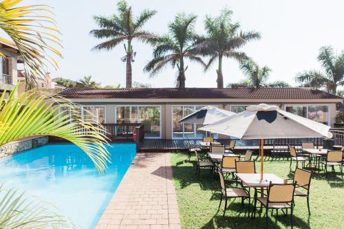 Umtentweni树下酒店及会议中心的房屋旁的游泳池配有椅子和遮阳伞