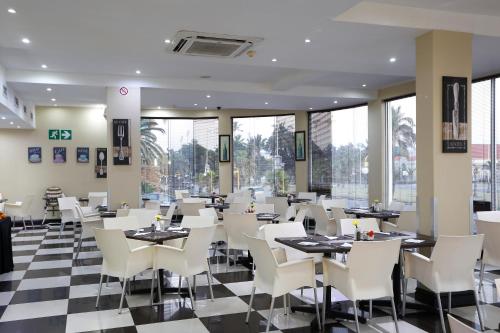 德班Pavilion Hotel Durban的餐厅设有白色的椅子和桌子以及窗户。