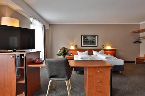 巴登-巴登Hotel Quellenhof的酒店客房配有一张带书桌的床铺和一台电视。