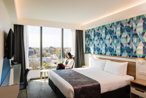 基督城Carnmore Hotel Christchurch的坐在酒店房间,有床和窗户的女人