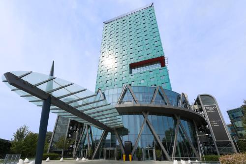 米兰voco Milan-Fiere, an IHG Hotel的一座高大的玻璃建筑,前面有楼梯