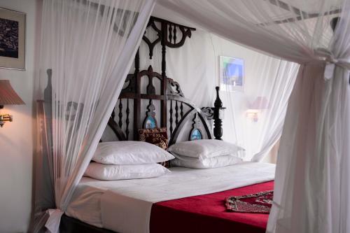 桑给巴尔特姆波豪斯酒店的卧室配有带白色床单和枕头的天蓬床。