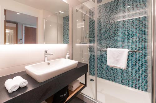 鲁瓦西昂法兰西Holiday Inn Paris CDG Airport an IHG Hotel的一间带水槽和玻璃淋浴的浴室
