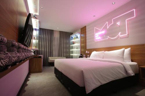 万隆Creative Restart Hotel - CARTEL Bandung的卧室配有一张大床,墙上挂着 ⁇ 虹灯标志