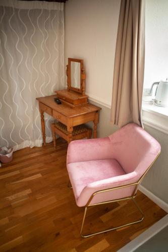 查格福德The Chagford Inn的一张粉红色的椅子,坐在一张桌子旁,带有镜子