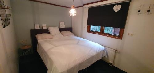DoornspijkChalet 11, in het bos的一间卧室配有一张带白色床单的床和一扇窗户。