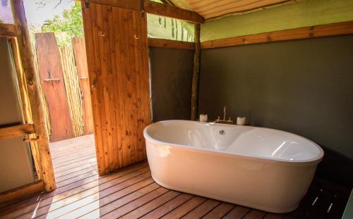 KhwaiO Bona Moremi Safari Lodge的浴室铺有木地板,设有大型白色浴缸。
