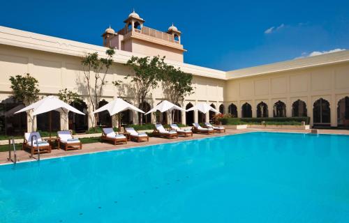 斋浦尔泰鼎浦尔酒店的一座带椅子和遮阳伞的大楼前的游泳池