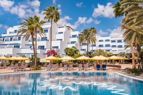 卡门港Seaside Los Jameos的酒店前方的游泳池配有椅子和遮阳伞