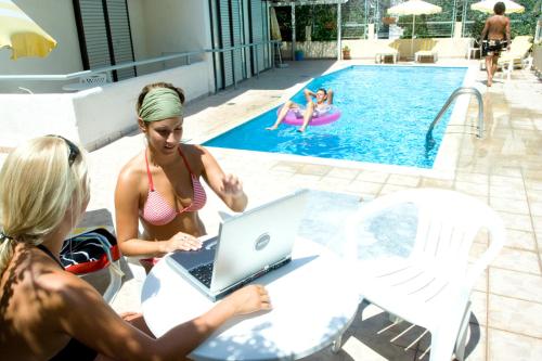 科斯镇伊斯伯利斯公寓式酒店的一群人坐在桌边,在游泳池边用笔记本电脑