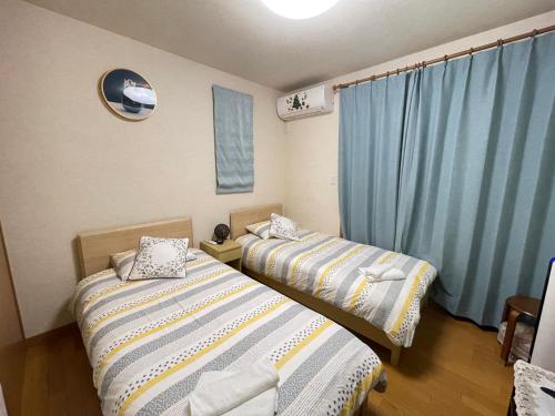 KashūMIKOTO HOUSE的配有蓝色窗帘的客房内的两张床