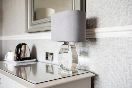彭里斯Roundthorn Country House & Luxury Apartments的玻璃桌上的一盏灯,上面有镜子