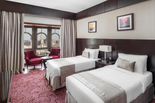 麦地那Taiba Front Hotel的酒店客房,设有两张床和一张红色椅子