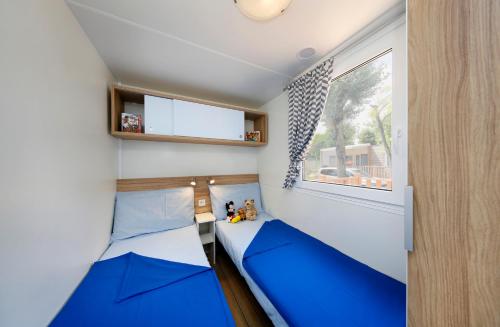 Porto FalconeraAlbatross Mobile Homes on Camping Laguna Village的小房间设有两张蓝色的床和窗户