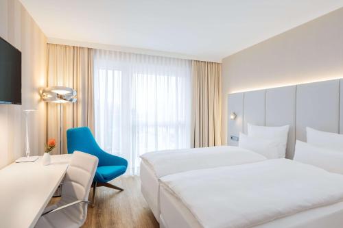 曼海姆NH Mannheim的酒店客房,设有两张床和一张蓝色椅子