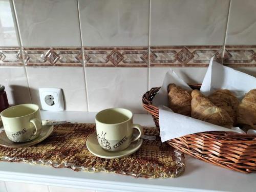 佩内拉Casa da Vitória的柜台上放两个咖啡杯和一篮面包