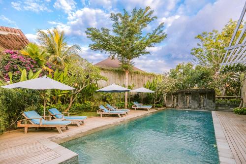 努沙杜瓦La Berceuse Resort and Villa Nusa Dua by Taritiya Collection的庭院内一个带椅子和遮阳伞的游泳池