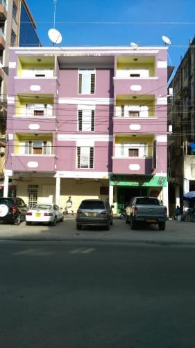 达累斯萨拉姆Kibodya Hotel Nkrumah的一座粉红色的建筑,前面有汽车停放