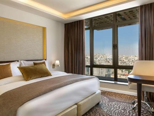 安曼Mövenpick Hotel Amman的一间卧室配有一张大床、一张书桌和窗户。