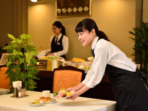 京都京都帕尔赛斯旅馆的站在餐桌上,拿着一盘食物的妇女