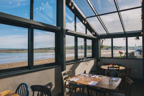 阿普尔多尔The Royal George的餐厅设有桌子和窗户,享有海滩美景