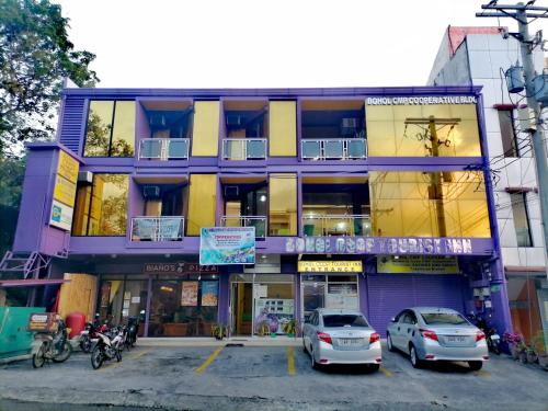塔比拉兰Bohol Coop Tourist Inn的一座紫色的建筑,前面有汽车停放