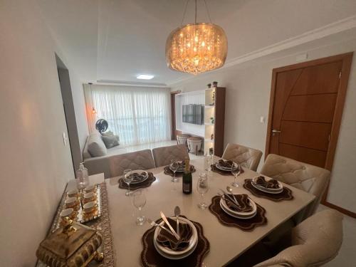 瓜拉派瑞Magnífico APARTAMENTO de Charme - 3 quartos AR CONDICIONADOS SPLIT - Beira Mar, 2 banheiros, 2 vagas garagem, 4 varandas, 2 elevadores, Redes para descanso, Wi-Fi, Air Fryer, Disney Plus, Star Plus, HBO Max, Guarda Sol, Cadeiras de Praia e Caixa Térmica的餐桌,配有盘子和酒杯