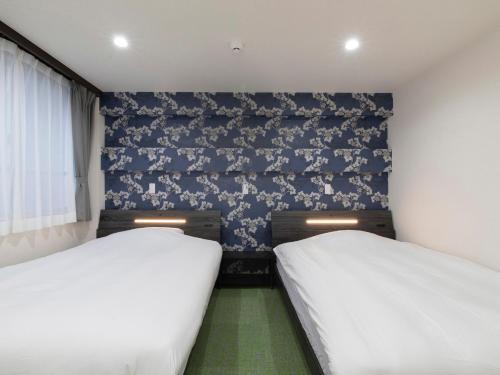 都城市Tabist Hotel Miyakonojo Miyazaki的小客房内的两张床,配以蓝色壁纸