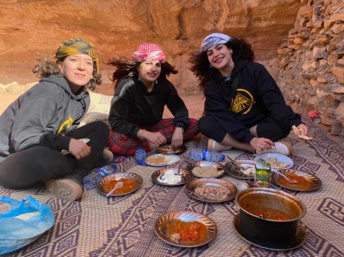 瓦迪拉姆Wadi Rum Cave Camp &Jeep Tour的一群三个女人坐在餐桌旁吃着食物