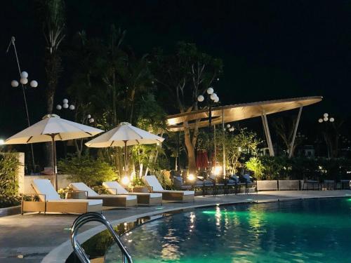 河静Songlam Waterfront Hotel的游泳池在晚上提供椅子和遮阳伞