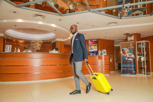 阿比让Hotel Tiama Abidjan的一个人在商店里拉着一个黄色的手提箱