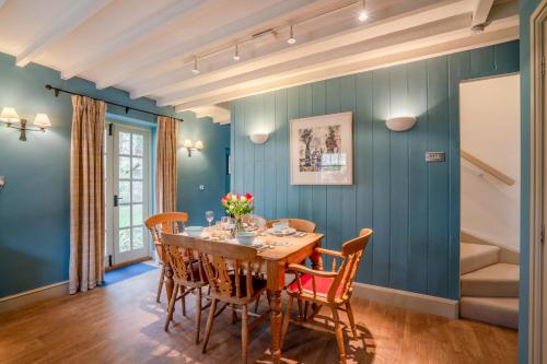 奇平卡姆登2 Manor Lodge Cottages的一间拥有蓝色墙壁和一张木桌及椅子的用餐室