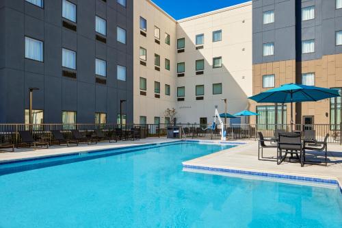 奥本Staybridge Suites - Auburn - University Area, an IHG Hotel的大楼前的带椅子和遮阳伞的游泳池