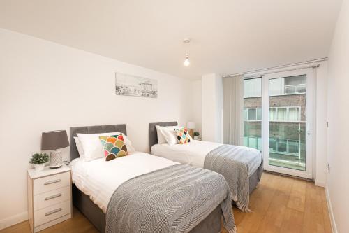 New BarnetSkyvillion - Station Road Apartment with Balcony & Parking的白色客房的两张床,设有窗户