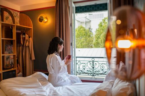 巴黎Hôtel Jardin de Cluny的坐在床上看着手机的女人