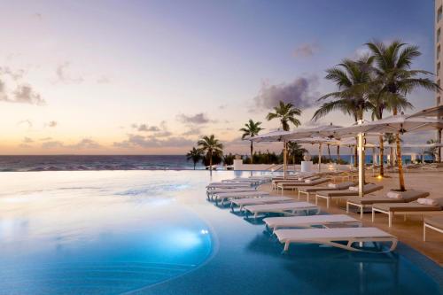 坎昆Le Blanc Spa Resort Cancun Adults Only All-Inclusive的海滩上带椅子和遮阳伞的酒店游泳池