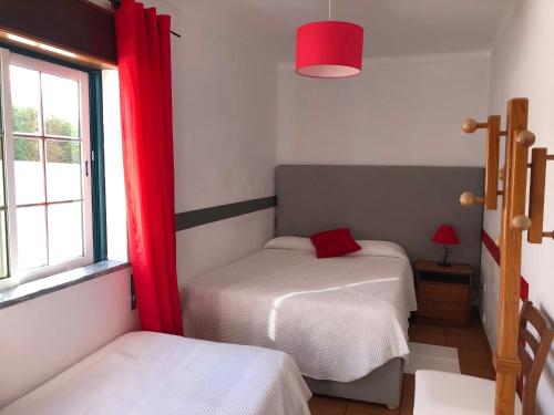 赞布热拉-杜马尔Camping Villa Park Zambujeira do Mar的一间卧室设有两张床,窗户配有红色窗帘