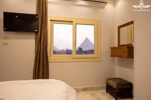 开罗Life Pyramids Inn的一间卧室设有一张床和一个享有金字塔美景的窗户。