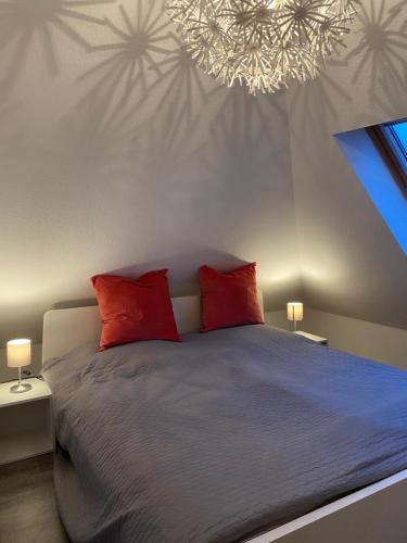 奈斯玛兹埃勒FeWo Herzstück - Neßmersiel的一间卧室配有一张带红色枕头的床和吊灯。