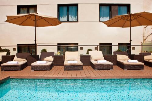 巴塞罗那格鲁普蒂尔格兰维亚678酒店的一座带椅子和遮阳伞的游泳池位于一座建筑旁边