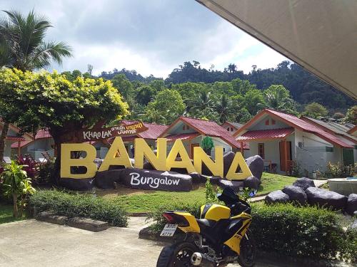 蔻立Khaolak Banana Bungalow的停在班纳纳标志前的摩托车