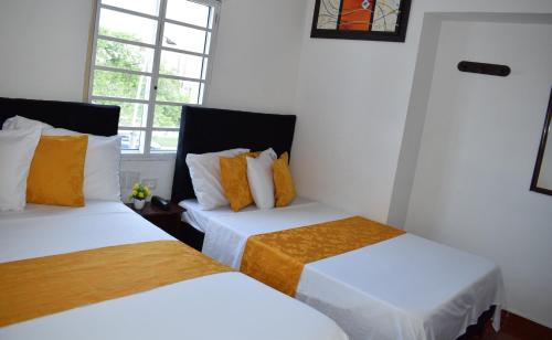 卡利Hotel Avenida 3 Real en el norte de Cali的配有白色和橙色枕头的客房内的两张床